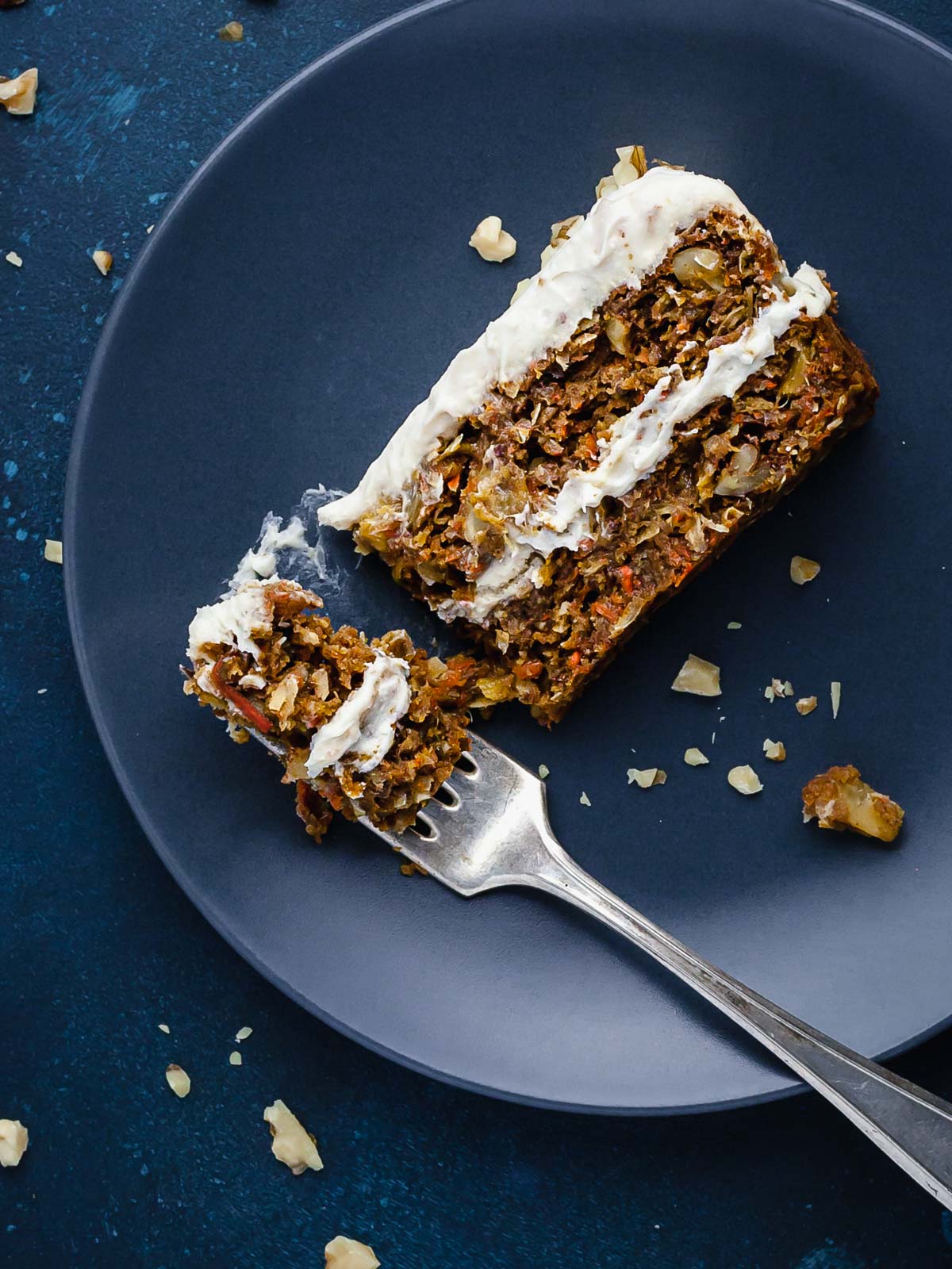 Overhead image of a slice of carrot cake on its side on a blue plate.