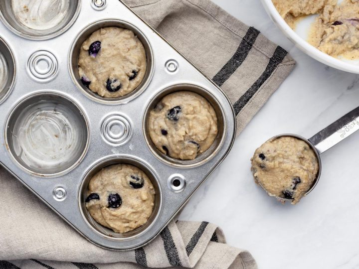 Overhead view of scooping blueberry muffin batter into a muffin tin.