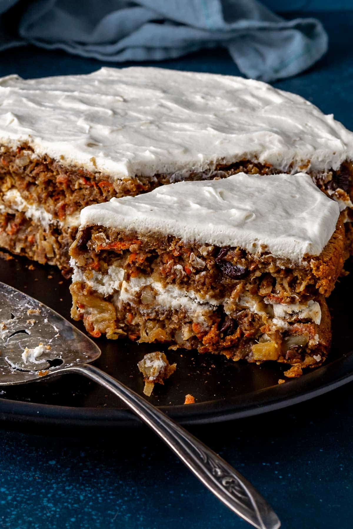 Close up side view of a slice of oat flour carrot cake with frosting on top and between the layers.