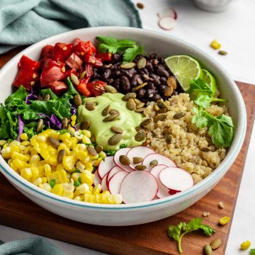 Mexican Buddha Bowl with quinoa, black beans, chopped tomato, steamed kale, purple cabbage, corn, sliced radishes, cilantro, and pepitas.