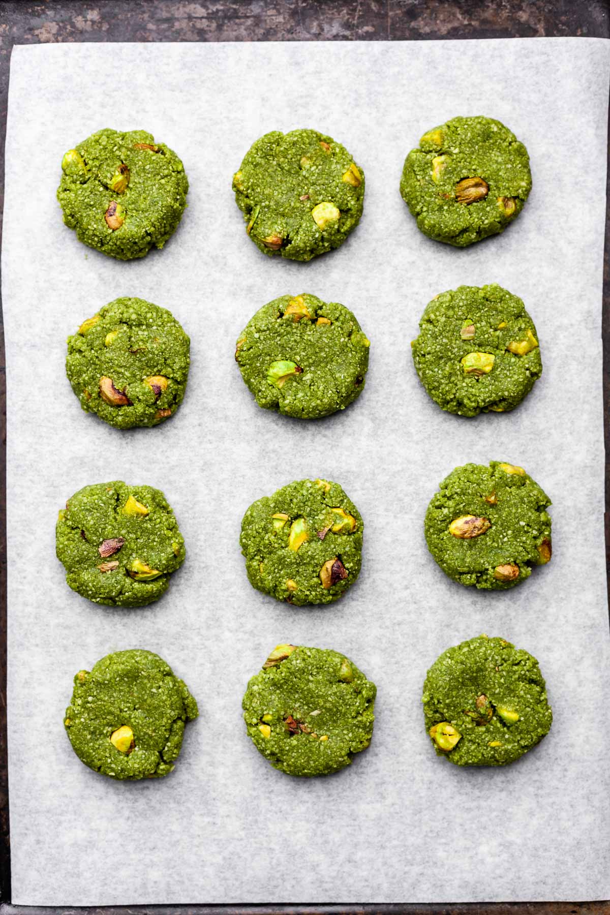 Overhead view of a parchment-lined cookie sheet with twelve evenly-spaced vegan matcha cookies before being baked.