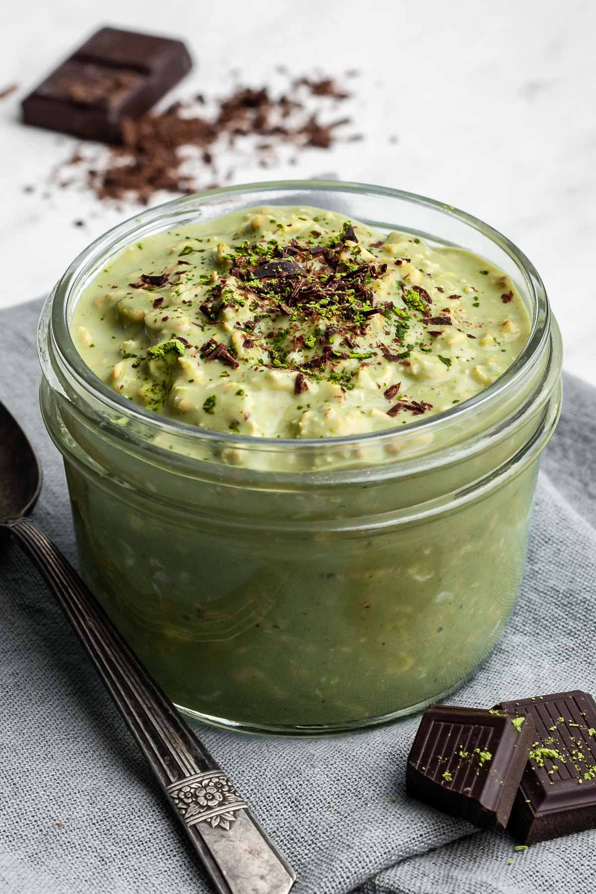 Jar of matcha oatmeal topped with shaved dark chocolate.