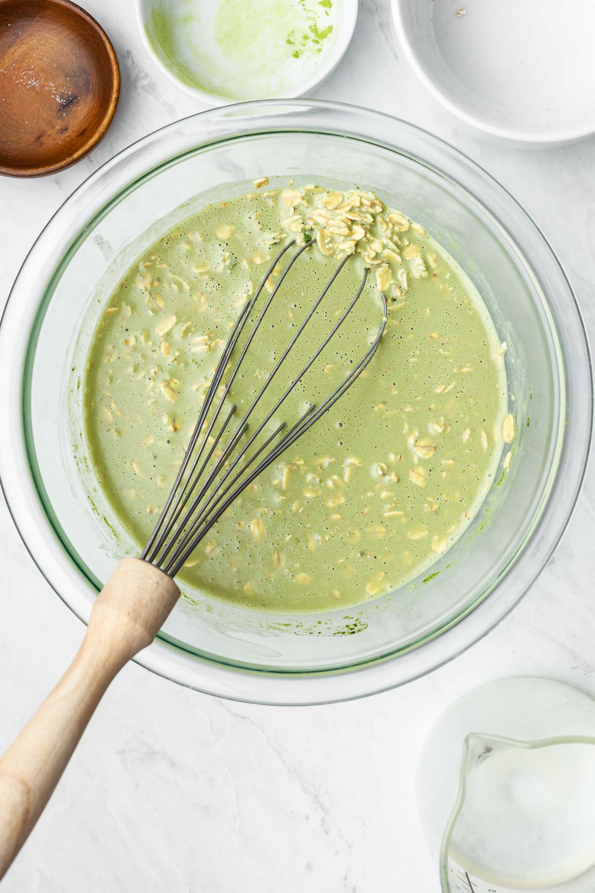 Bowl of matcha overnight oats with a wire whisk resting on the edge of the bowl.