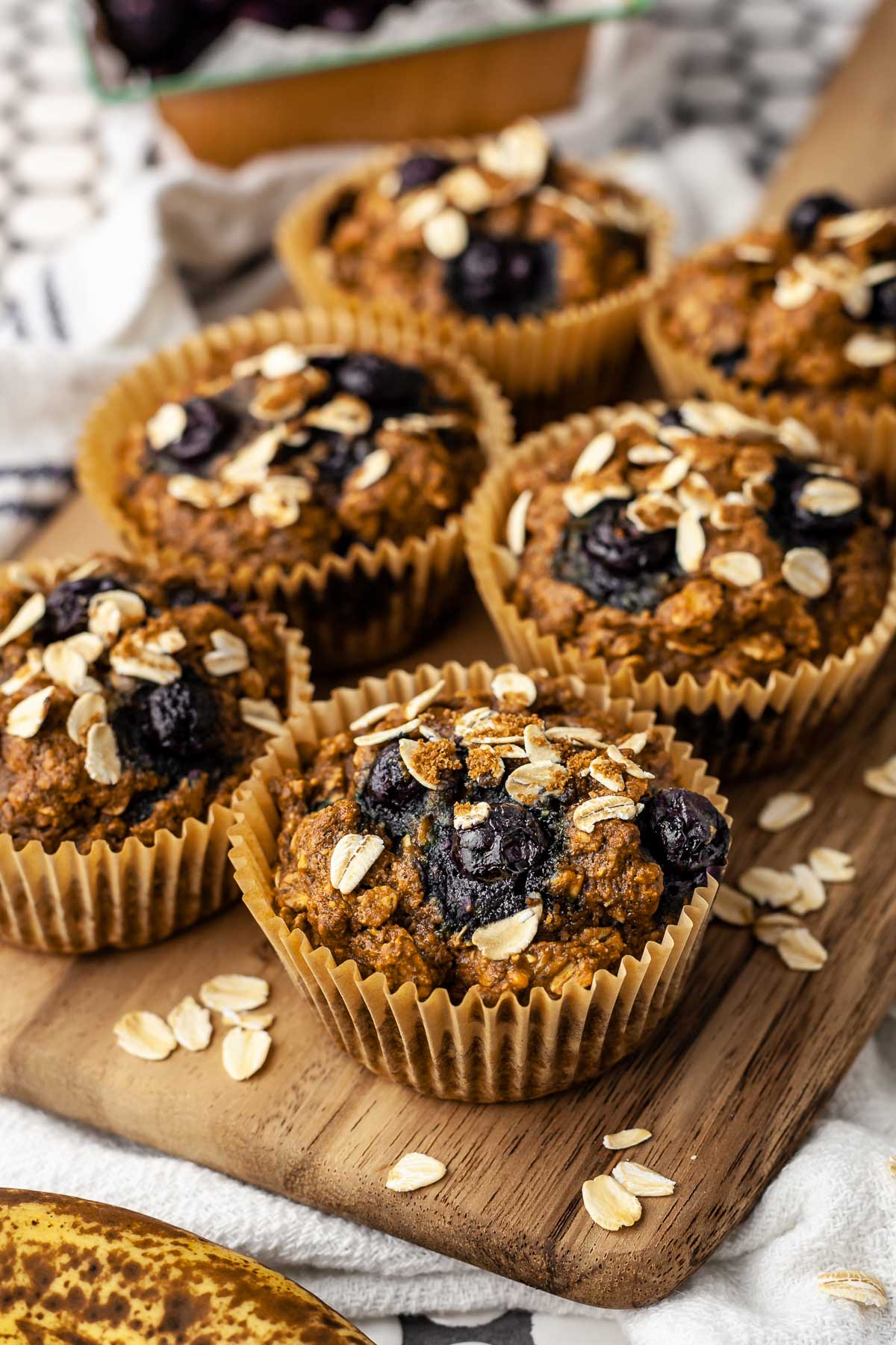 Six blueberry banana oatmeal muffins on a wooden cutting board.