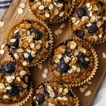 Overhead view of six blueberry banana oatmeal muffins on a wooden cutting board.
